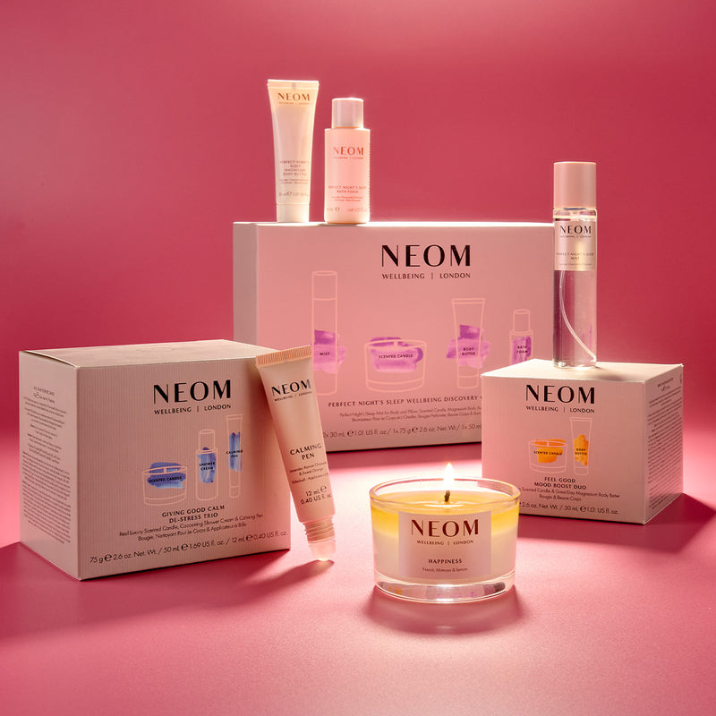 NEOM skincare products including bottles, boxes, and a candle on a pink background