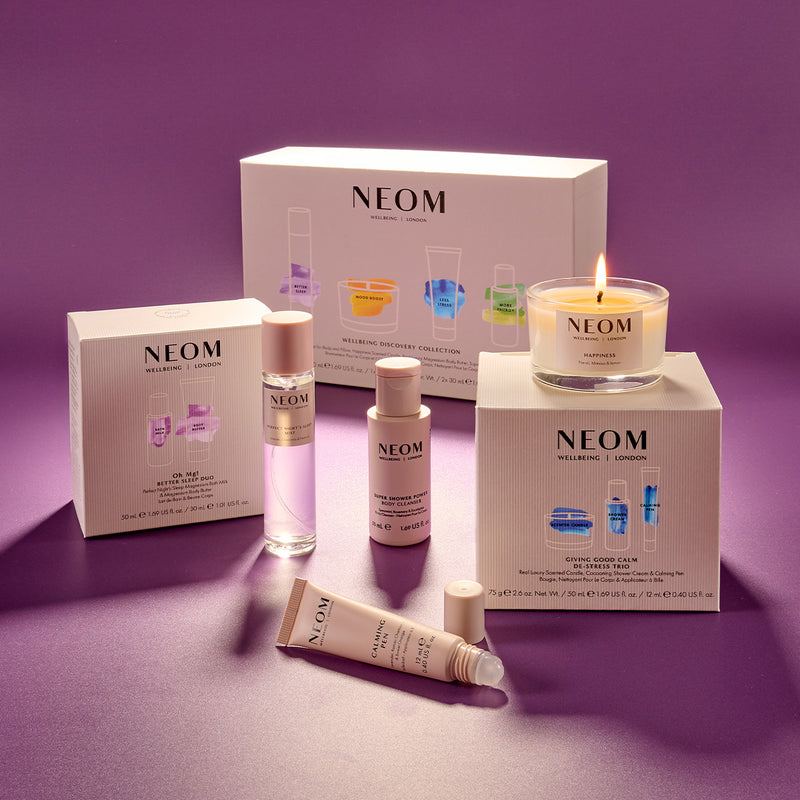 Neom skincare products including bottles, a candle, and boxes on a purple background