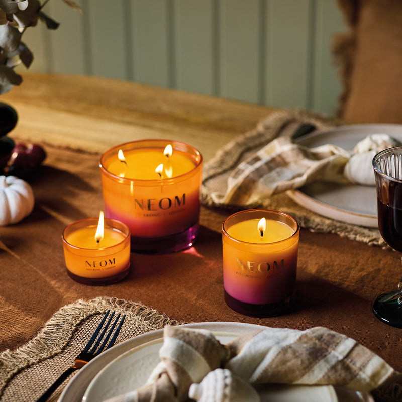NEOM candles on a table with a warm setting