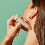 Woman applying NEOM Energy Pen to her neck against a green background
