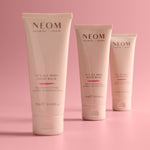 Three Neom hand balms on a pink background