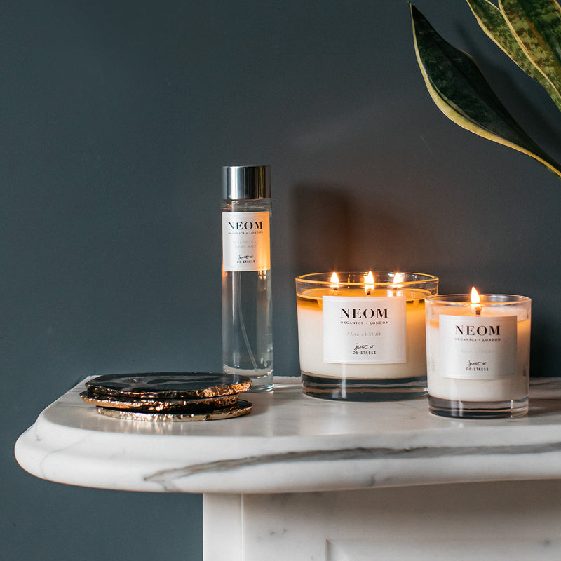 NEOM products including a bottle and two candles on a marble surface with a dark background.